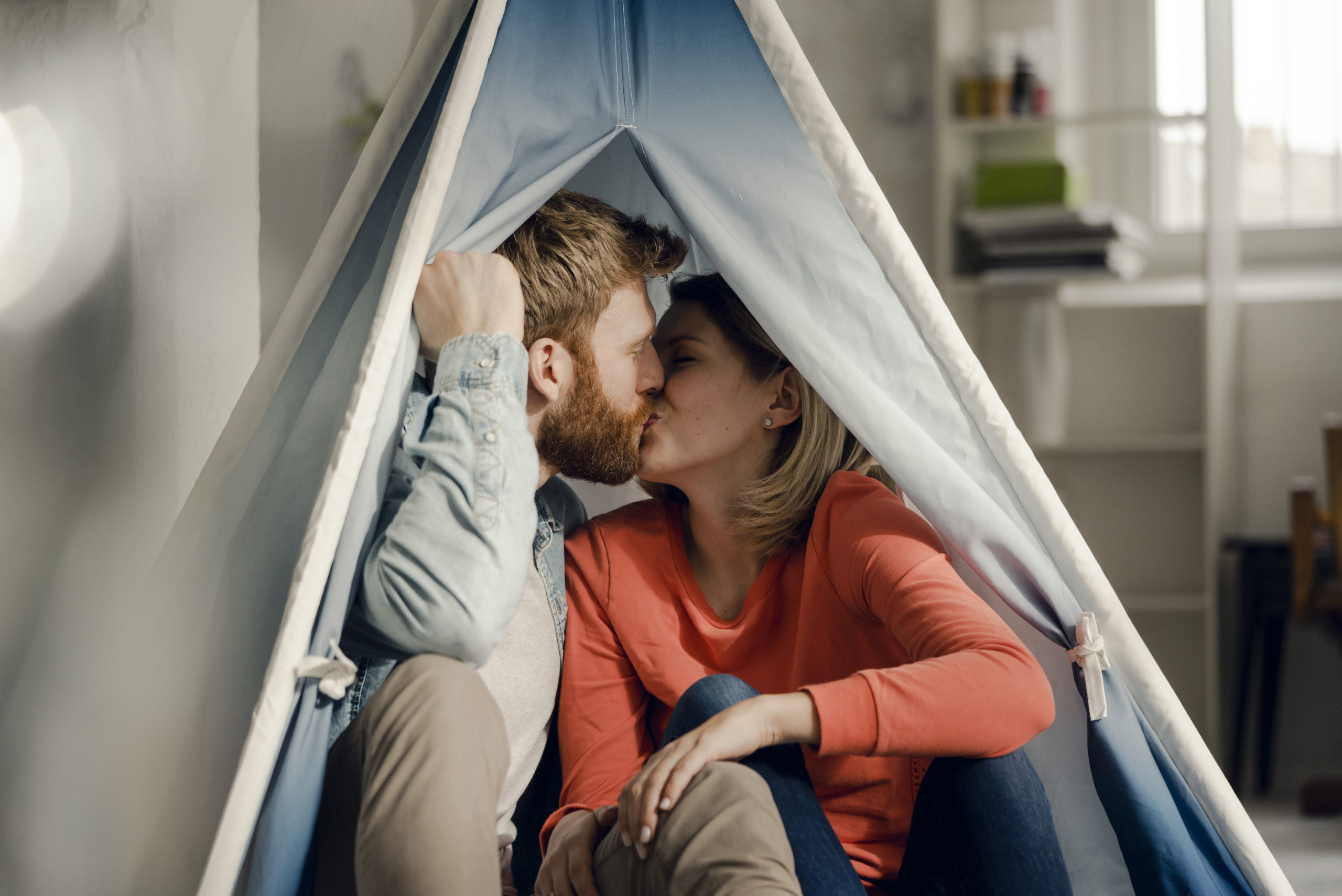 Happy couple at home sitting in a romantic setting and kissing after talking about the topic of dating vs. relationships.