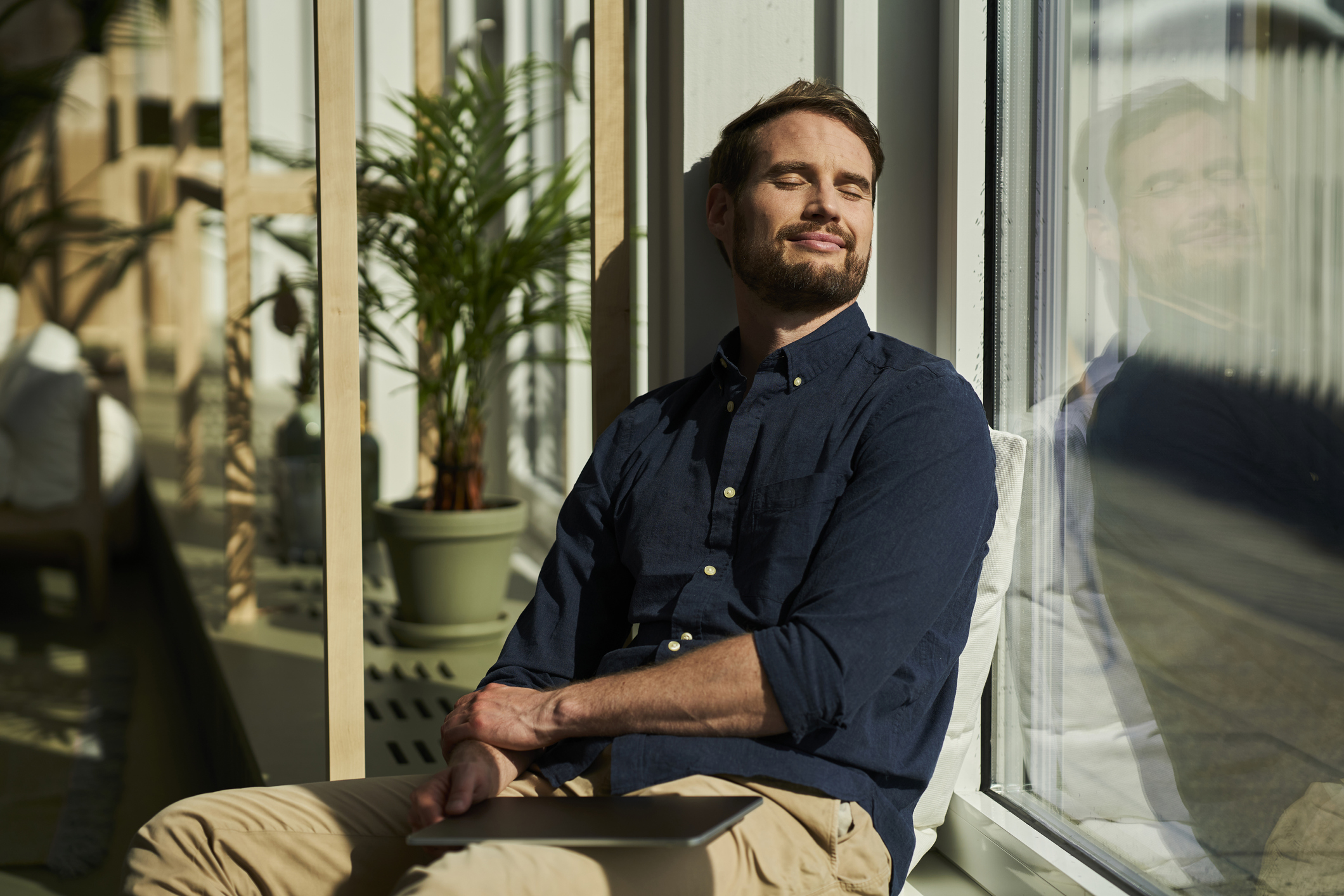 Smiling professional man, leaning against the window with eyes closed and contemplating after reading a list of quotes about letting go.