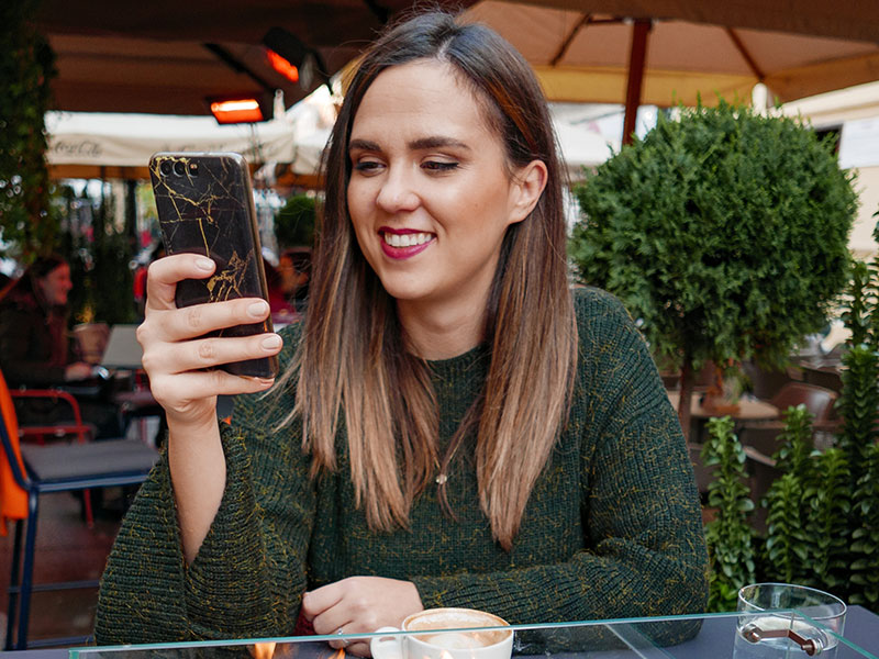A woman receiving cute texts for her from the guy she likes and smiling while she's drinking coffee.