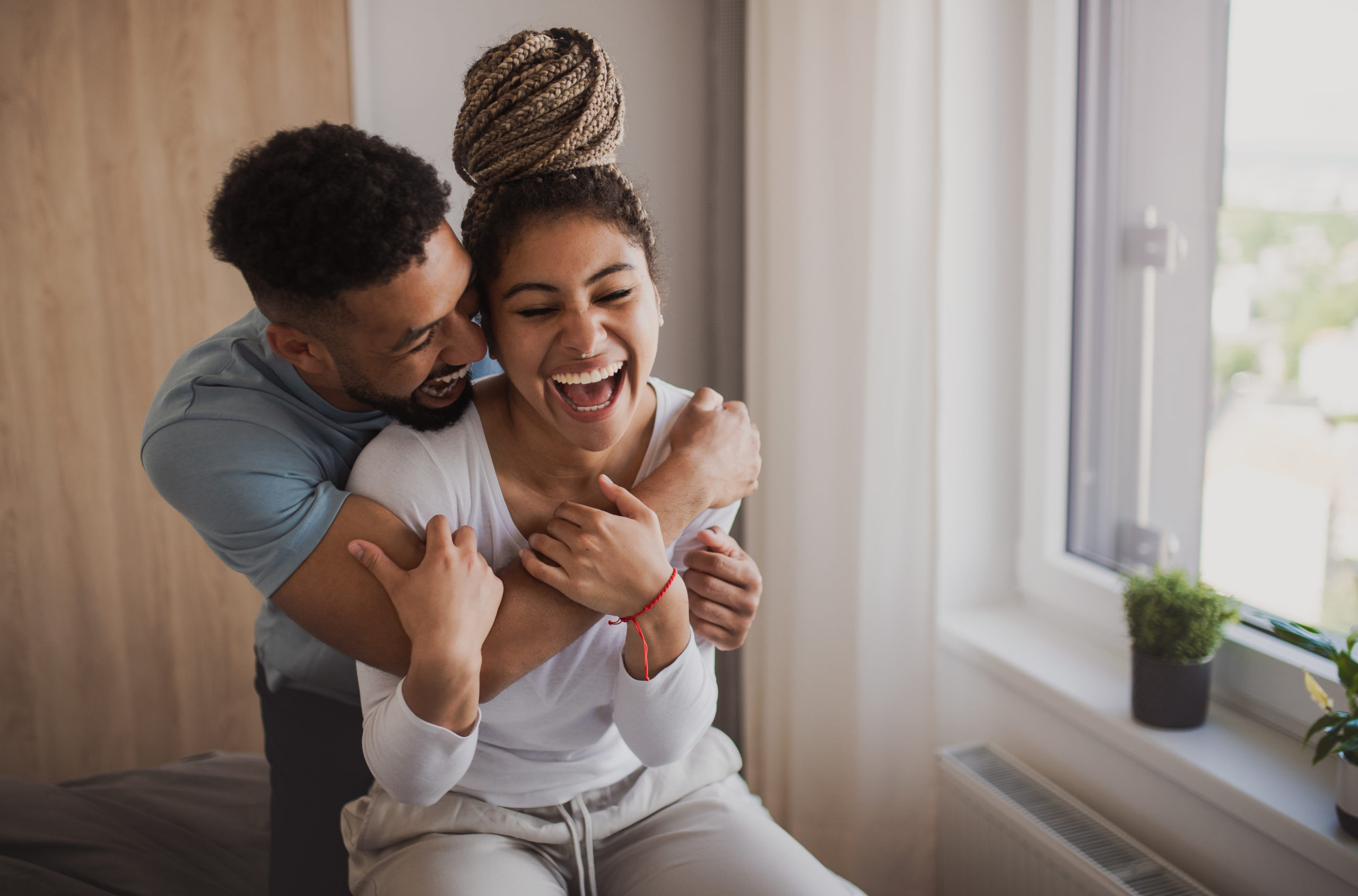 Young, happy couple laughing and embracing each other while trying out some of the best quality time love language ideas.