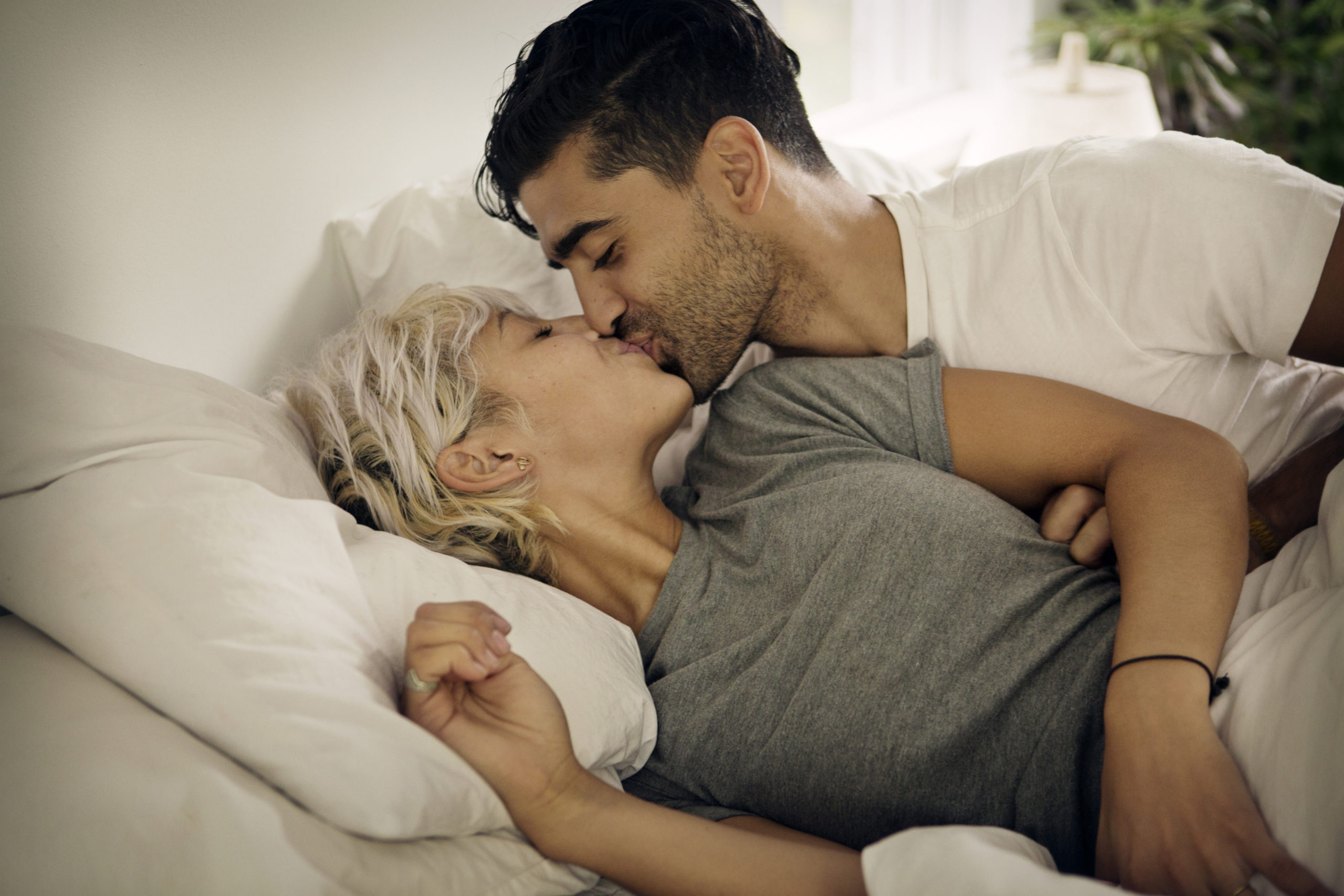 Happy couple lying in bed at home smiling and kissing after she sent a romantic goodnight text for him.
